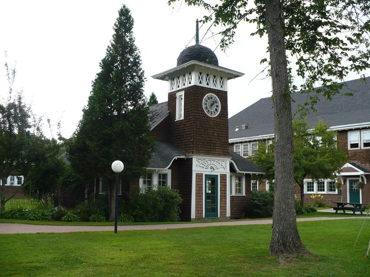 A scenic view of Goddard College's Clockhouse, surrounded by greenery and a historic building in the background.